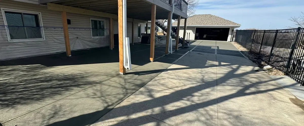 Fresh concrete patio installation under elevated deck at residential home with modern railing system