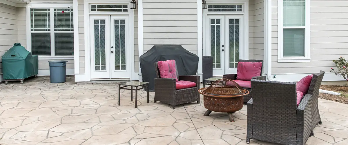 Stamped concrete patio with outdoor seating, fire pit, and grill setup against light siding home